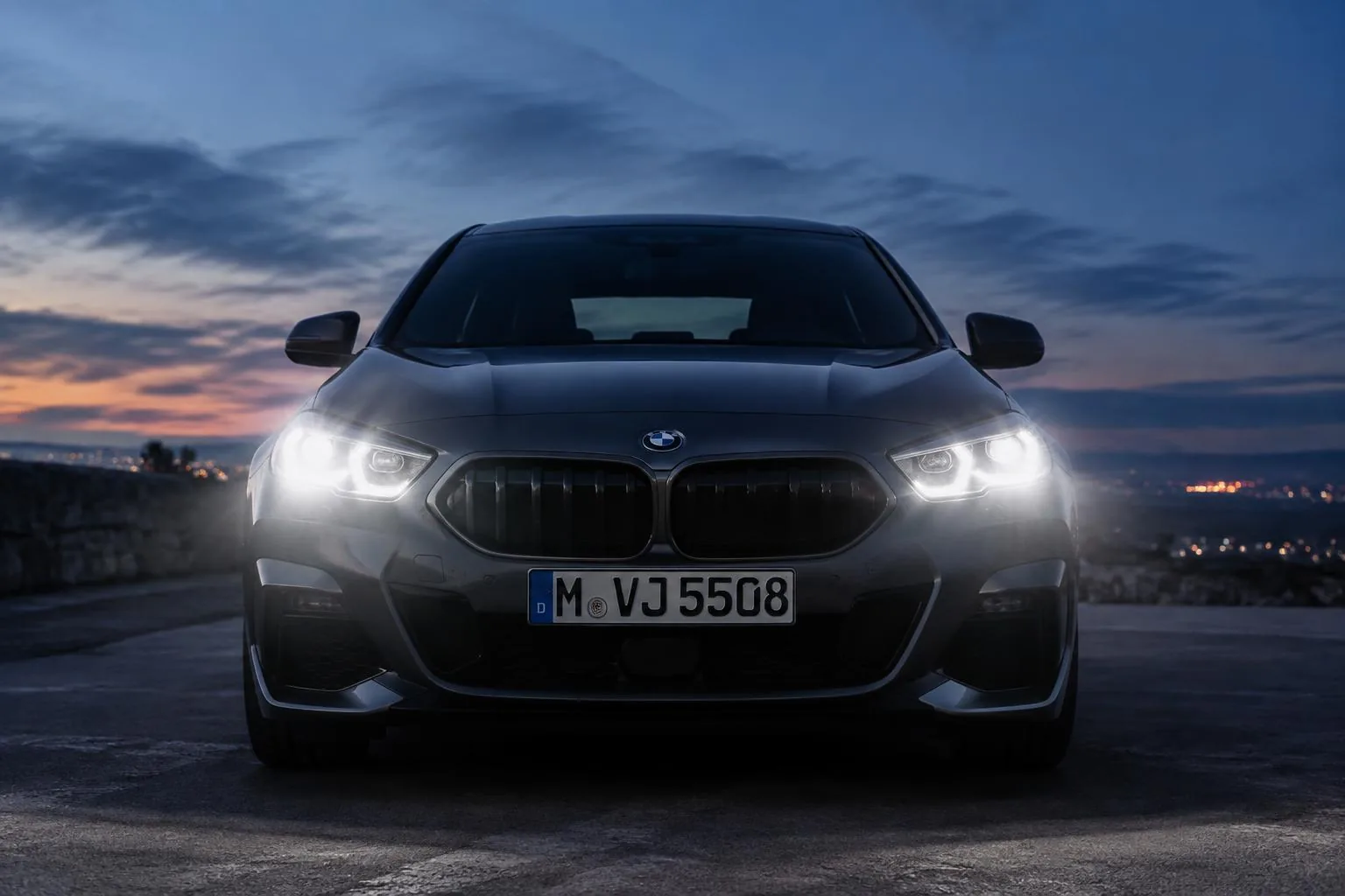 Coche visto de frente al atardecer con los faros LED encendidos iluminando la carretera